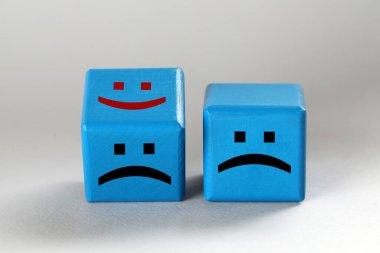 Light blue cubes with sad and happy faces on light grey background clipart