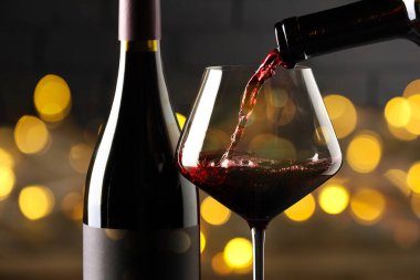 Kırmızı şarabı bardağa ve şişeye doldurup karanlık arka planda bulanık ışıklarla, yakın plan. Bokeh etkisi