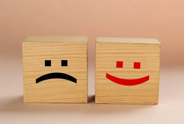 Wooden cubes with sad and happy faces on beige background