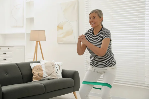 Senior woman doing squats with fitness elastic band at home