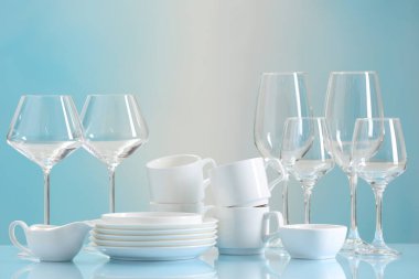 Açık mavi masada bir sürü temiz bulaşık takımı ve bardak var.