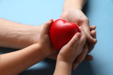 Baba ve çocuğu açık mavi arka planda kırmızı dekoratif kalp taşıyor, yakın plan.