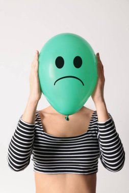 Woman hiding behind green balloon with sad face on white background clipart