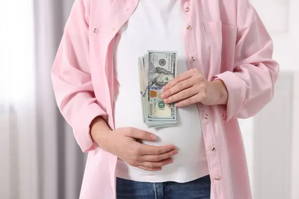 Surrogate mother. Pregnant woman with dollar banknotes indoors, closeup