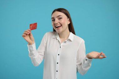 Açık mavi arka planda kredi kartı olan mutlu bir kadın.