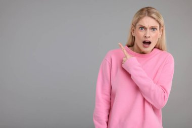 Gri arkaplandaki bir şeyi işaret eden şaşırmış kadın, mesaj için yer