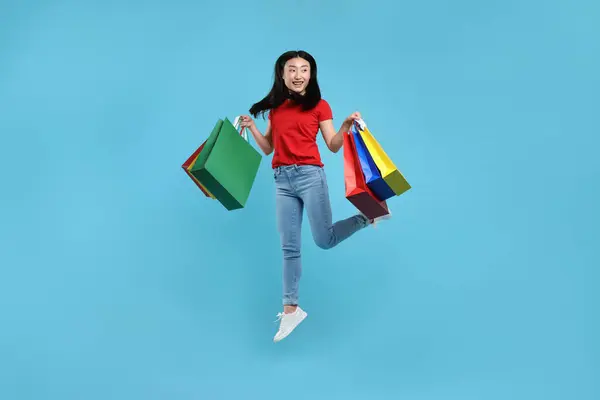 Mujer Feliz Saltando Con Bolsas Compras Sobre Fondo Azul Claro —  Fotos de Stock