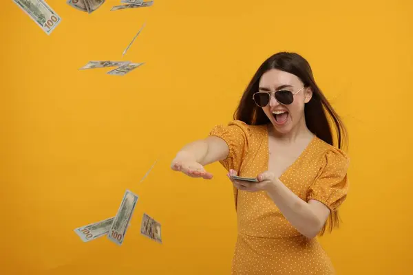 Happy woman throwing money on orange background