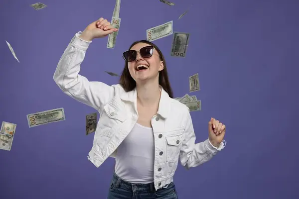 Happy woman under money shower on purple background