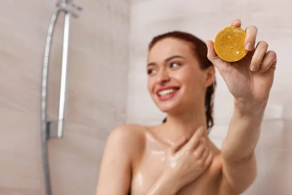 Happy young woman with solid shampoo bar in shower, selective focus. Space for text