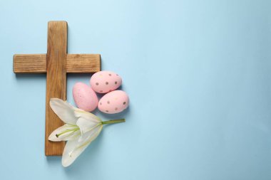 Ahşap haç, Paskalya yumurtaları ve açık mavi arka planda zambak çiçeği, üst manzara. Metin için boşluk