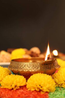 Diwali kutlaması. Diya lambası, renkli rangoli ve kasımpatı çiçekleri karanlık arka planda, yakın plan. Metin için boşluk