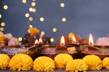Diwali kutlaması. Diya lambaları ve kasımpatı çiçekleri bulanık ışıklara karşı masada, yakın plan