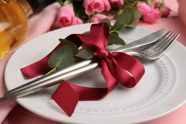 Romantic place setting. Plate, cutlery, eucalyptus branch and roses on table, closeup