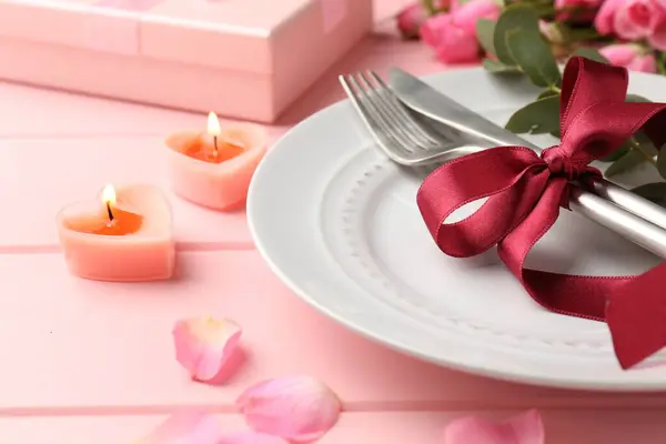 Place setting with roses and candles on pink table, closeup. Romantic dinner