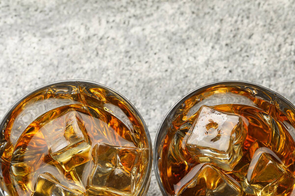 Whiskey and ice cubes in glasses on grey textured table, top view. Space for text