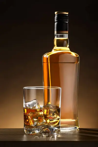 木のテーブルのガラスとボトルの氷の立方体が付いているウイスキー — ストック写真