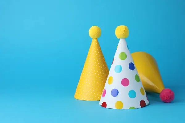 Colorful party hats on light blue background, space for text