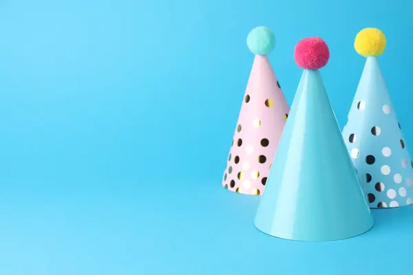 Colorful party hats on light blue background, space for text