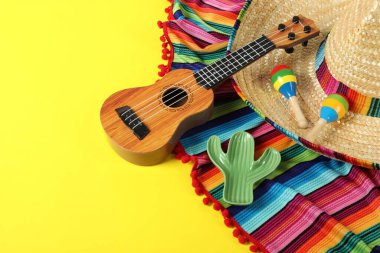 Meksika şapkalı kompozisyon, ukulele ve marakas sarı masada, yakın plan. Metin için boşluk