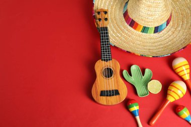 Kırmızı arka planda Meksika şapkası ve ukulele ile düz kompozisyon. Metin için boşluk
