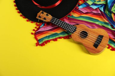 Siyah Flamenko şapka, panço ve ukulele sarı masada, manzaranın üstünde. Metin için boşluk