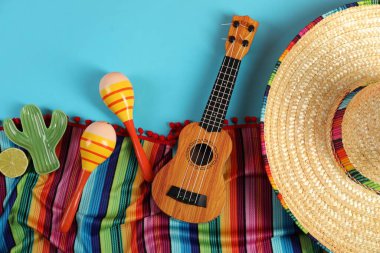 Meksika şapkası, marakas ve ukulele ile açık mavi masa üzerinde düz kompozisyon