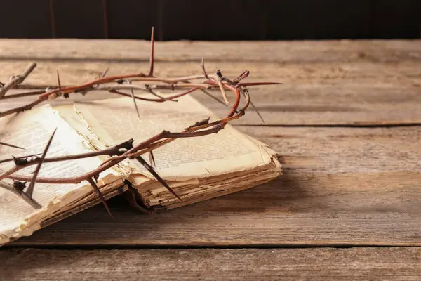 Crown of thorns and Bible on wooden table, closeup. Space for text