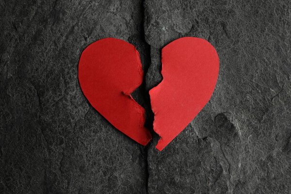 Halves of torn red paper heart on dark grey table, top view. Broken heart