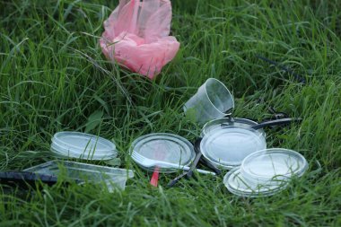 Dışarıdaki çimlerin üzerinde plastik sofra takımı ve poşet kullanılmış. Çevre kirliliği kavramı