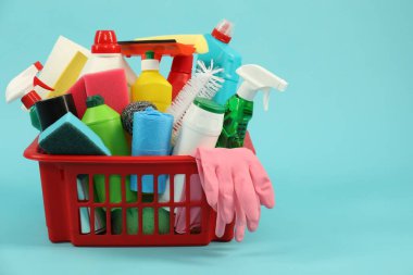 Açık mavi arkaplanda plastik sepette farklı temizlik ürünleri, metin için alan