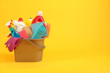 Sarı arkaplanda kovadaki farklı temizlik ürünleri, metin için yer