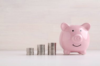 Finansal tasarruflar. Domuz kumbarası ve beyaz ahşap masaya istiflenmiş paralar.