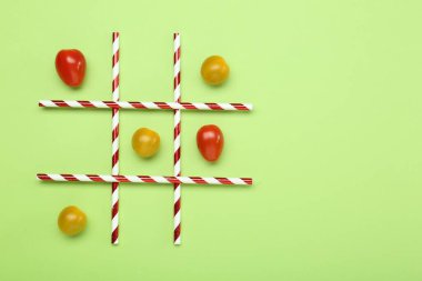 Açık yeşil arka planda vişneli domateslerle yapılan tik tak parmak oyunu, üst görünüm