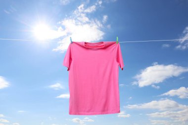 Mavi gökyüzüne karşı çamaşır ipinde kuruyan pembe tişört.