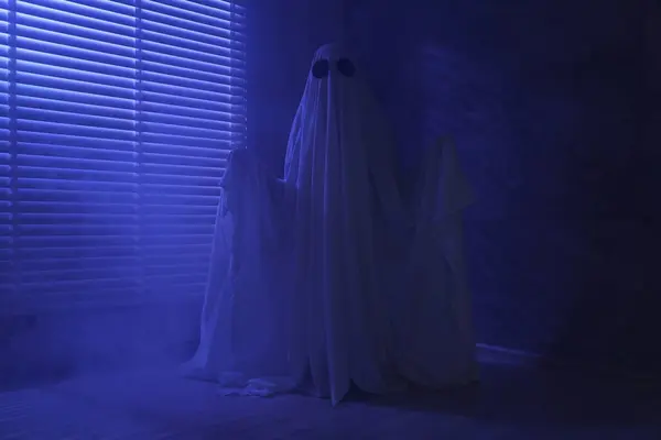Creepy ghost. Woman covered with sheet near window in blue light