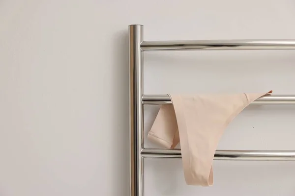 Heated towel rail with beige underwear on white wall, closeup. Space for text