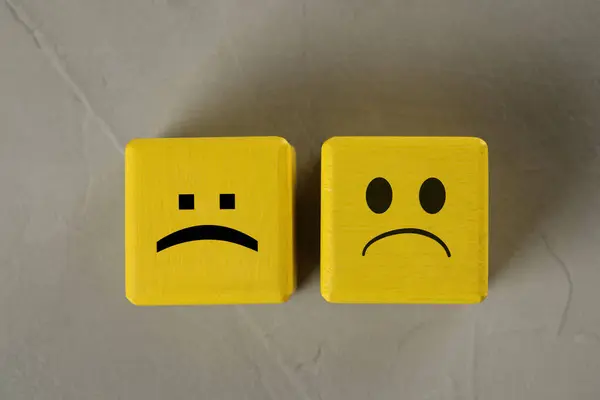 Yellow cubes with sad faces on grey table, top view
