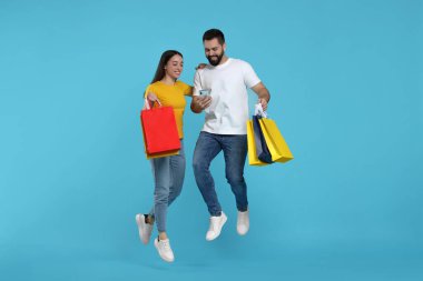 Alışveriş çantalı mutlu çift ve açık mavi arka planda atlayan akıllı telefon.