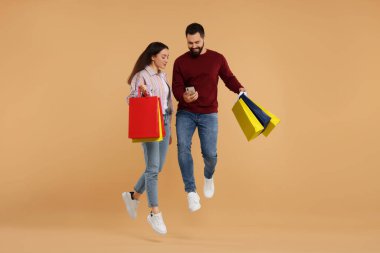 Alışveriş çantalı mutlu çift ve bej arka planda atlayan akıllı telefon.
