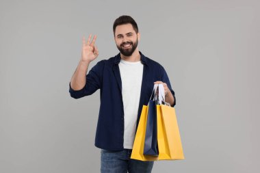 Bir sürü kağıt torbası olan mutlu bir adam gri arka planda iyi niyet gösterisi yapıyor.