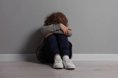 Çocuk istismarı. Üzgün çocuk gri duvarın yanında oturuyor.