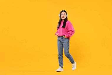 Turuncu arka planda kulaklıklı gülümseyen kadın portresi. Metin için boşluk