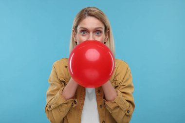 Açık mavi arka planda balon şişiren kadın