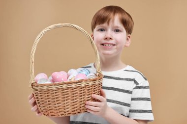 Paskalya kutlaması. Hasır sepeti koyu bej arka planda boyalı yumurtalarla dolu şirin bir çocuk.