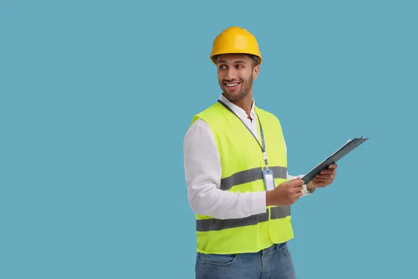 stock image Engineer in hard hat holding clipboard on light blue background, space for text