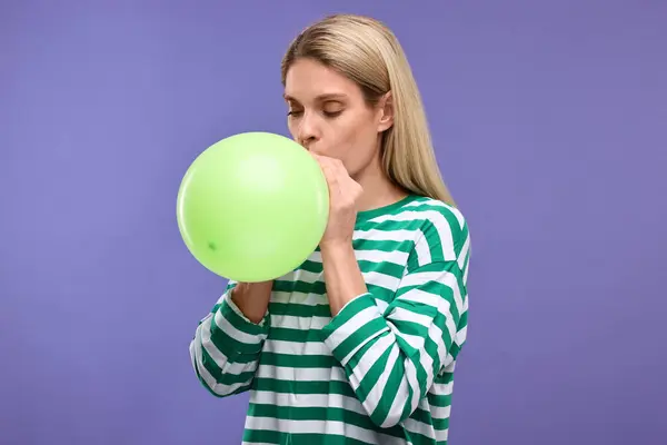 stock image Woman blowing up balloon on violet background