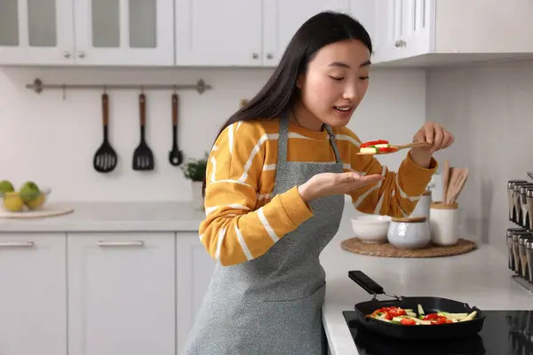 stock image Beautiful woman cooking and tasting vegetable dish in kitchen. Space for text