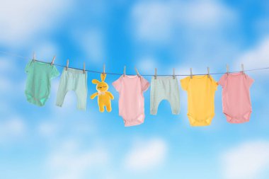 Baby clothes and crochet toy drying on washing line against sky