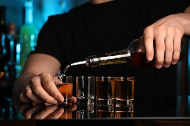 Barmen bardaki ayna tezgahında bardağa içki dolduruyor, yakın plan.